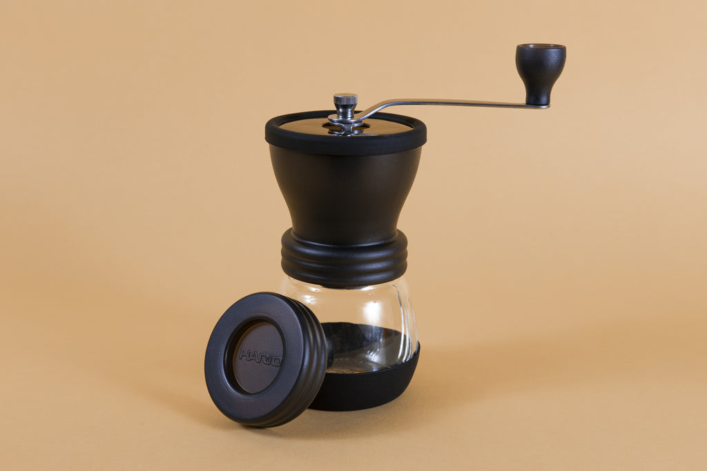 Black plastic coffee mill with handle attached to a glass container via screw top with a rubber base, and plastic lid.