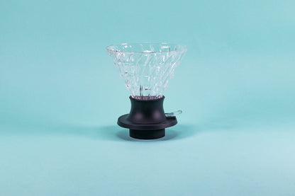 Large cone-shaped glass dripper with black silicone base with clear plastic switch on a light blue background.