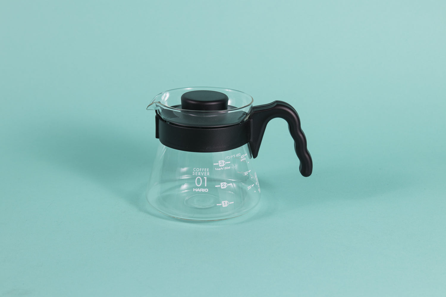 Glass coffee server with white text and level markings with black hard plastic handle and lid on a teal background.