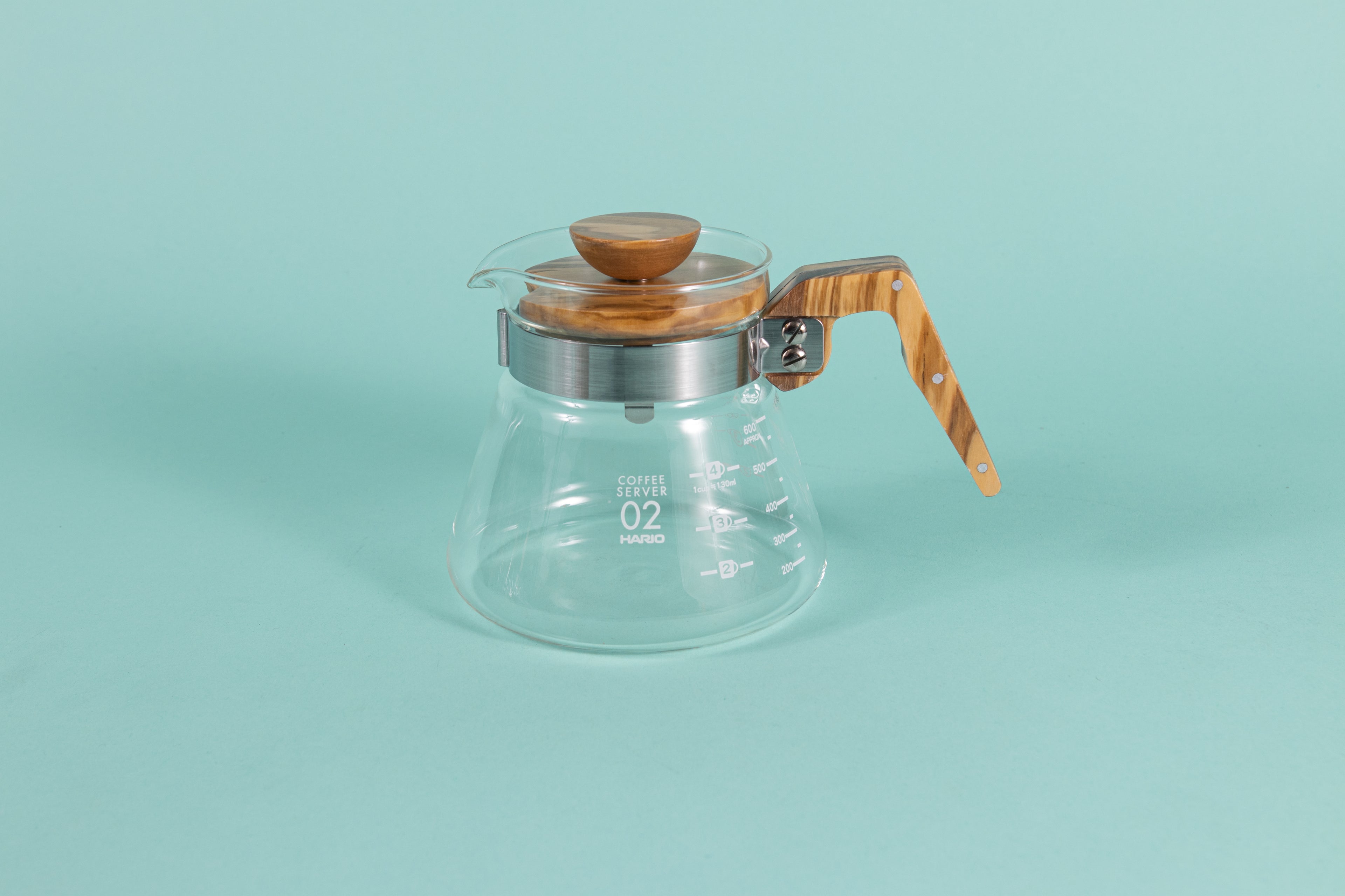 Glass coffee server with white text and markings with a brushed metal collar and wooden handle and lid on a teal backdrop.