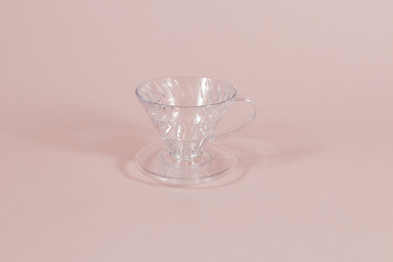 Clear all plastic cone shaped dripper with handle and round base on a pink backdrop.