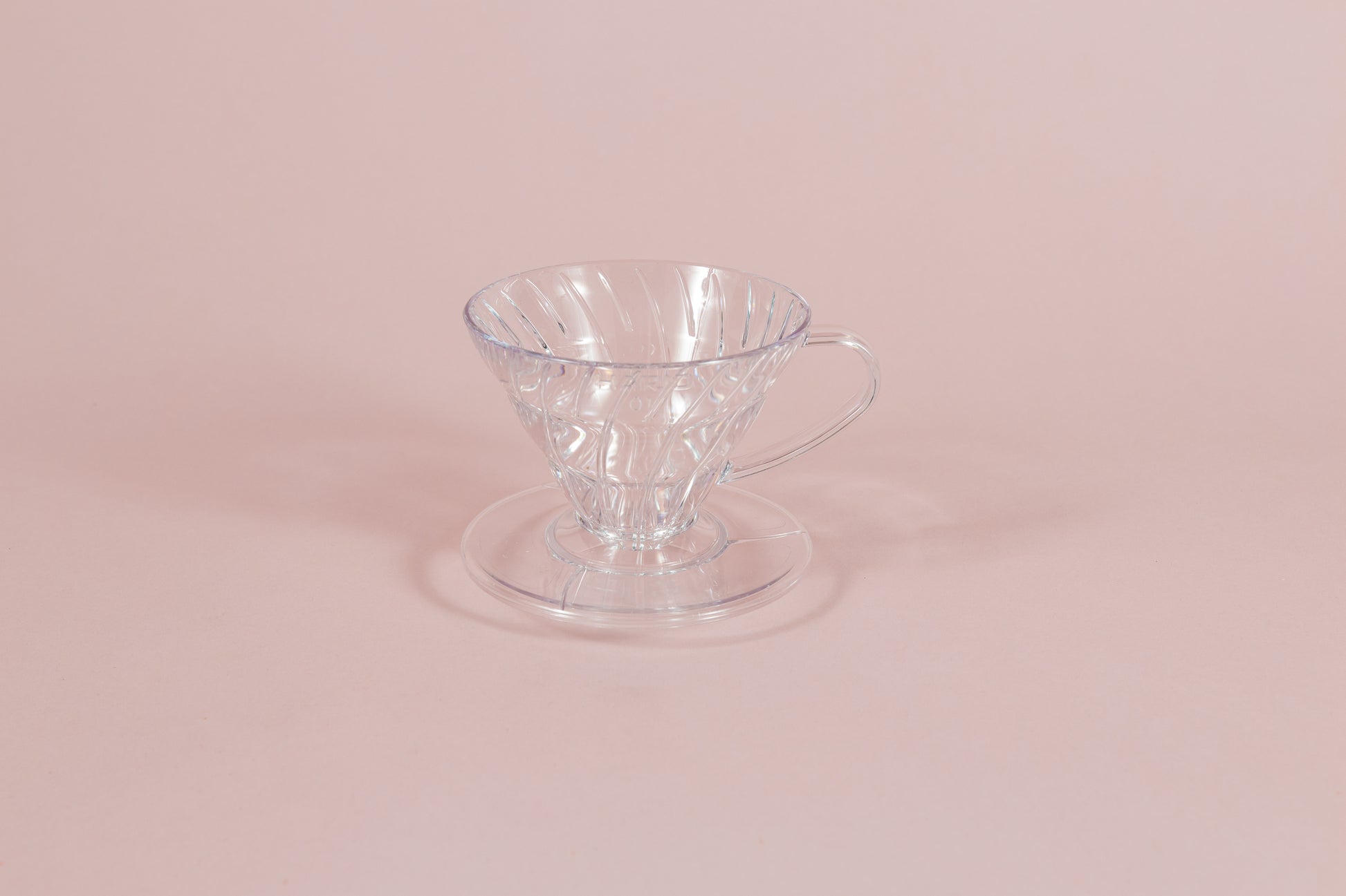 Clear all plastic cone shaped dripper with handle and round base on a pink backdrop.