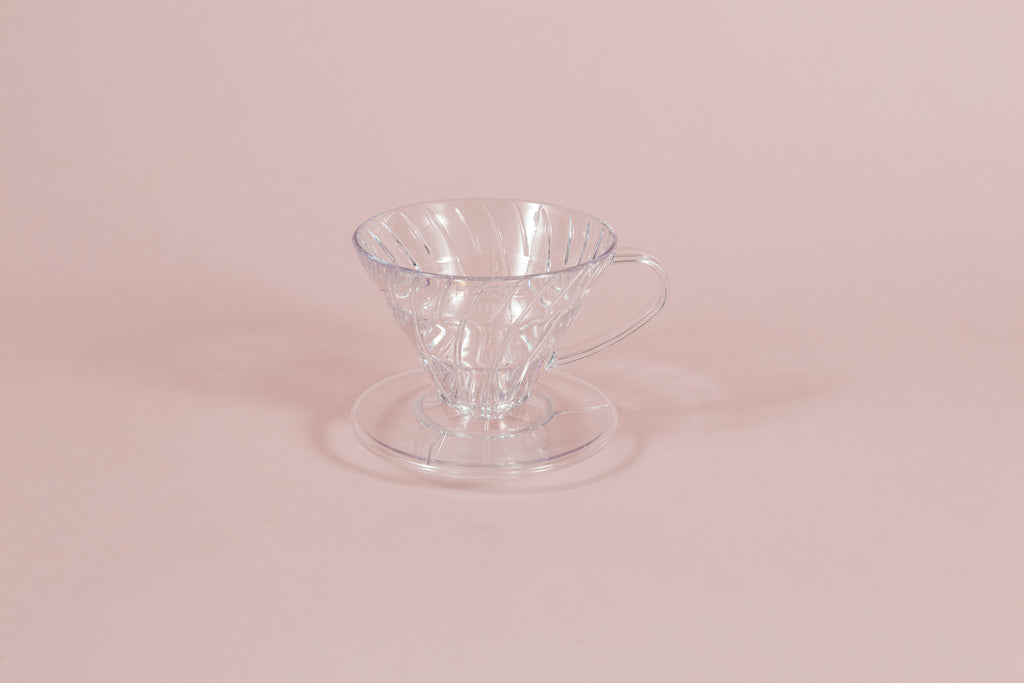 Clear all plastic cone shaped dripper with handle and round base on a pink backdrop.