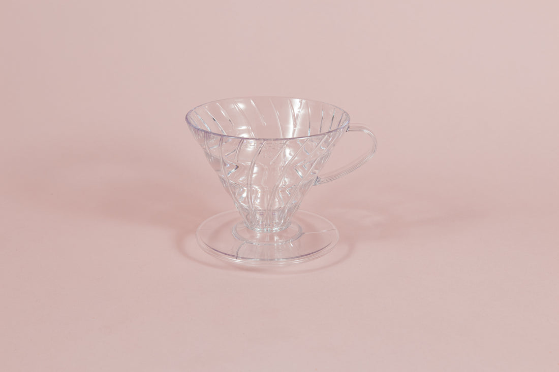 Clear all plastic cone shaped dripper with handle and round base on a pink backdrop.