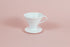 White all plastic cone shaped dripper with handle and round base on a pink backdrop.