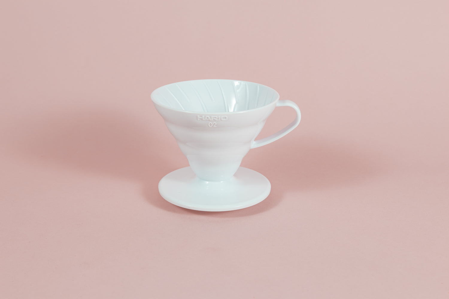 White all plastic cone shaped dripper with handle and round base on a pink backdrop.