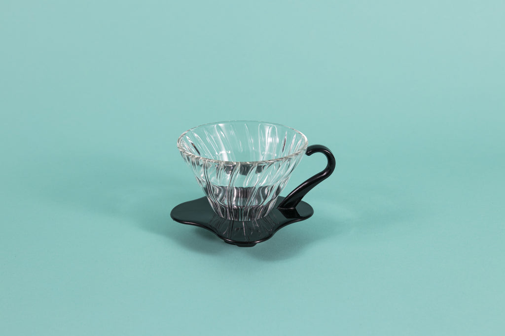 Clear all glass cone shaped coffee dripper with ribs, sitting in a black plastic base and handle.