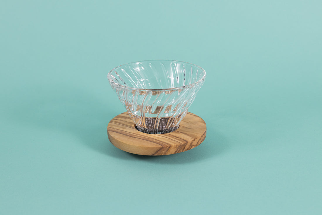 Clear all glass cone shaped coffee dripper with ribs, sitting in a round olive wood base.