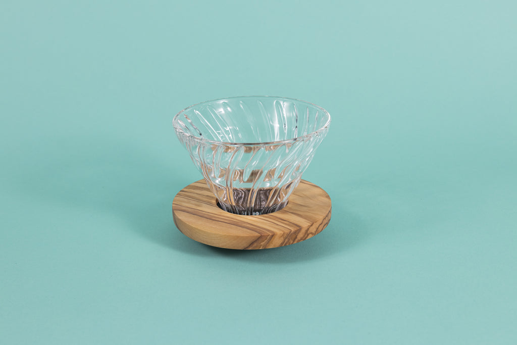 Clear all glass cone shaped coffee dripper with ribs, sitting in a round olive wood base.