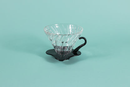 Clear all glass cone shaped coffee dripper with ribs, sitting in a black plastic base and handle.