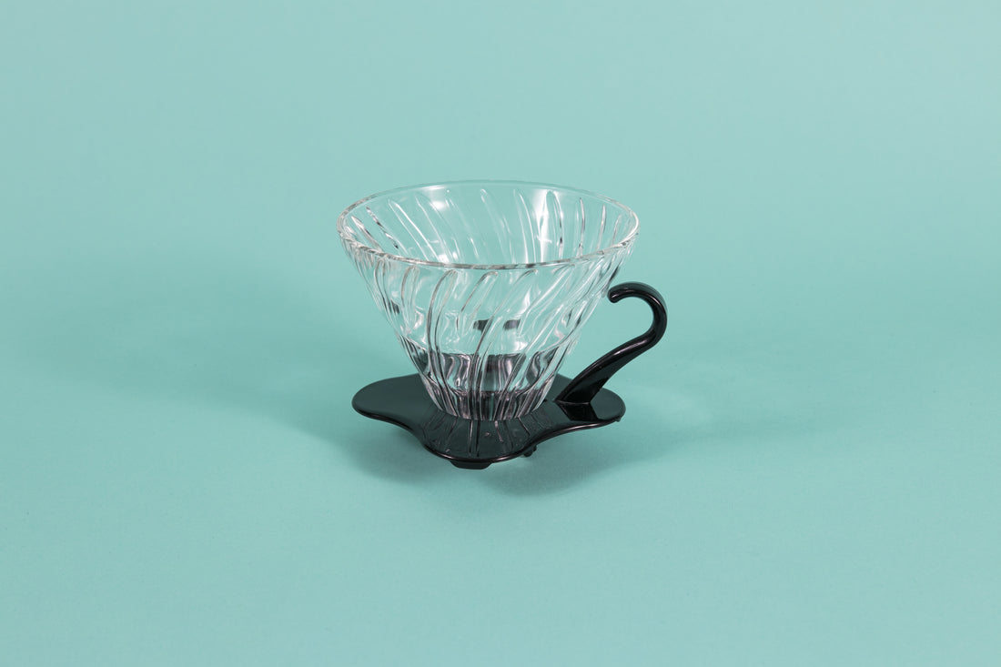 Clear all glass cone shaped coffee dripper with ribs, sitting in a black plastic base and handle.