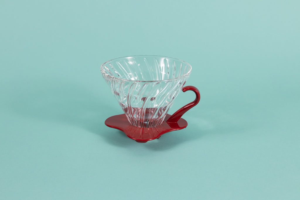 Clear all glass cone shaped coffee dripper with ribs, sitting in a red plastic base and handle.