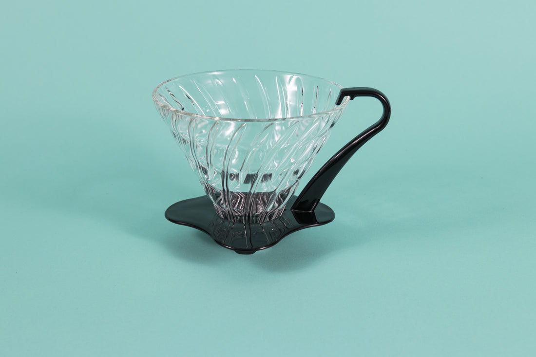 Large clear all glass cone shaped coffee dripper with ribs, sitting in a black plastic base and handle.