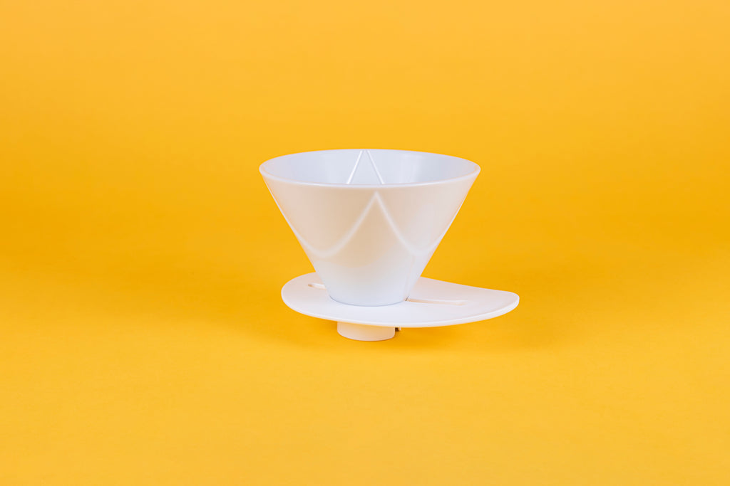 White plastic cone shaped dripper with bezier ridges and oval shaped white plastic base on a yellow background.