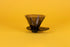 Translucent black plastic cone shaped dripper with bezier ridges and oval shaped black plastic base on a yellow background.