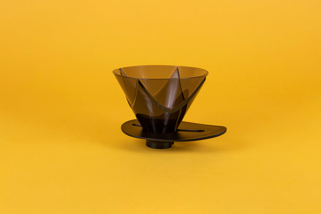 Translucent black plastic cone shaped dripper with bezier ridges and oval shaped black plastic base on a yellow background.
