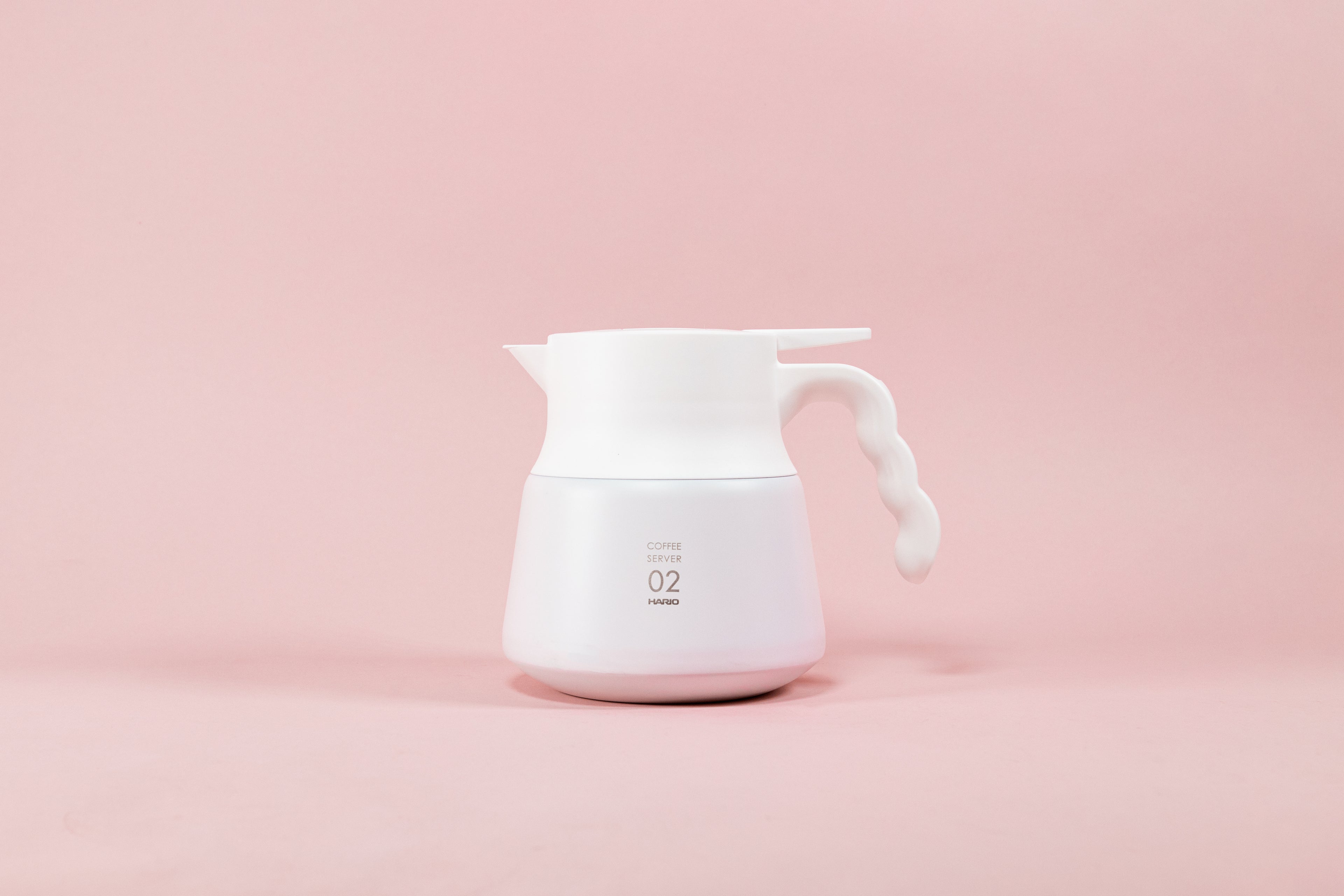 White matte coffee server with white plastic wavy handle on a pink background.
