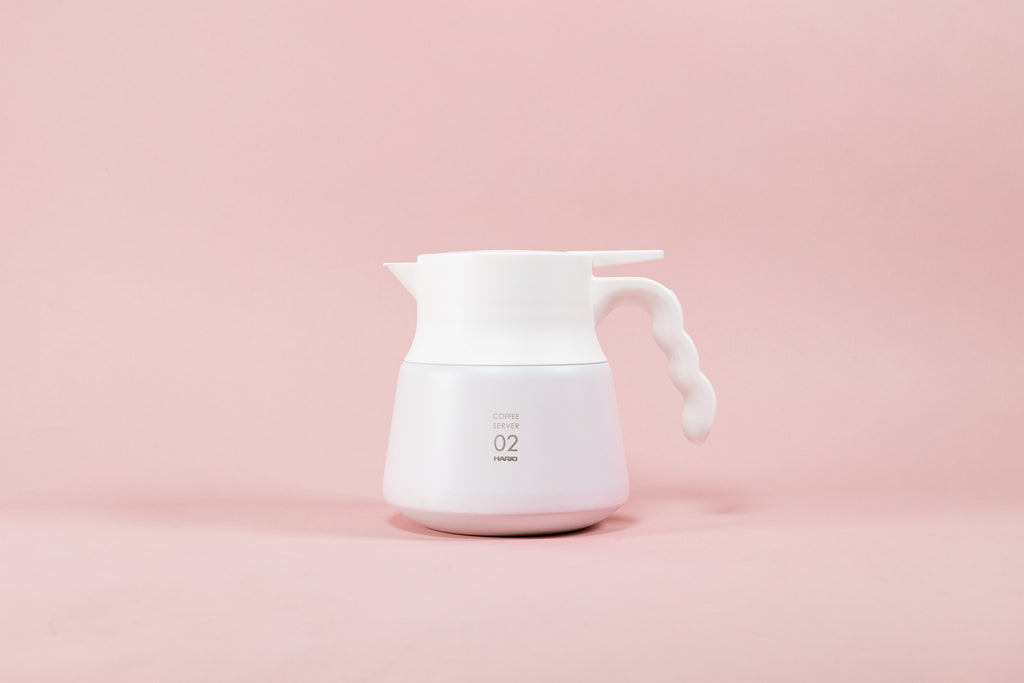 White matte coffee server with white plastic wavy handle on a pink background.