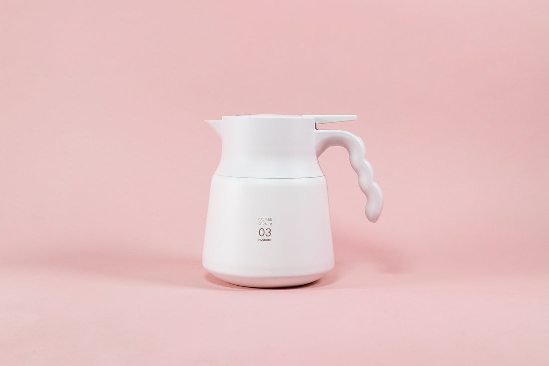 Matte white coffee server with wavy white plastic handle on a pink background.
