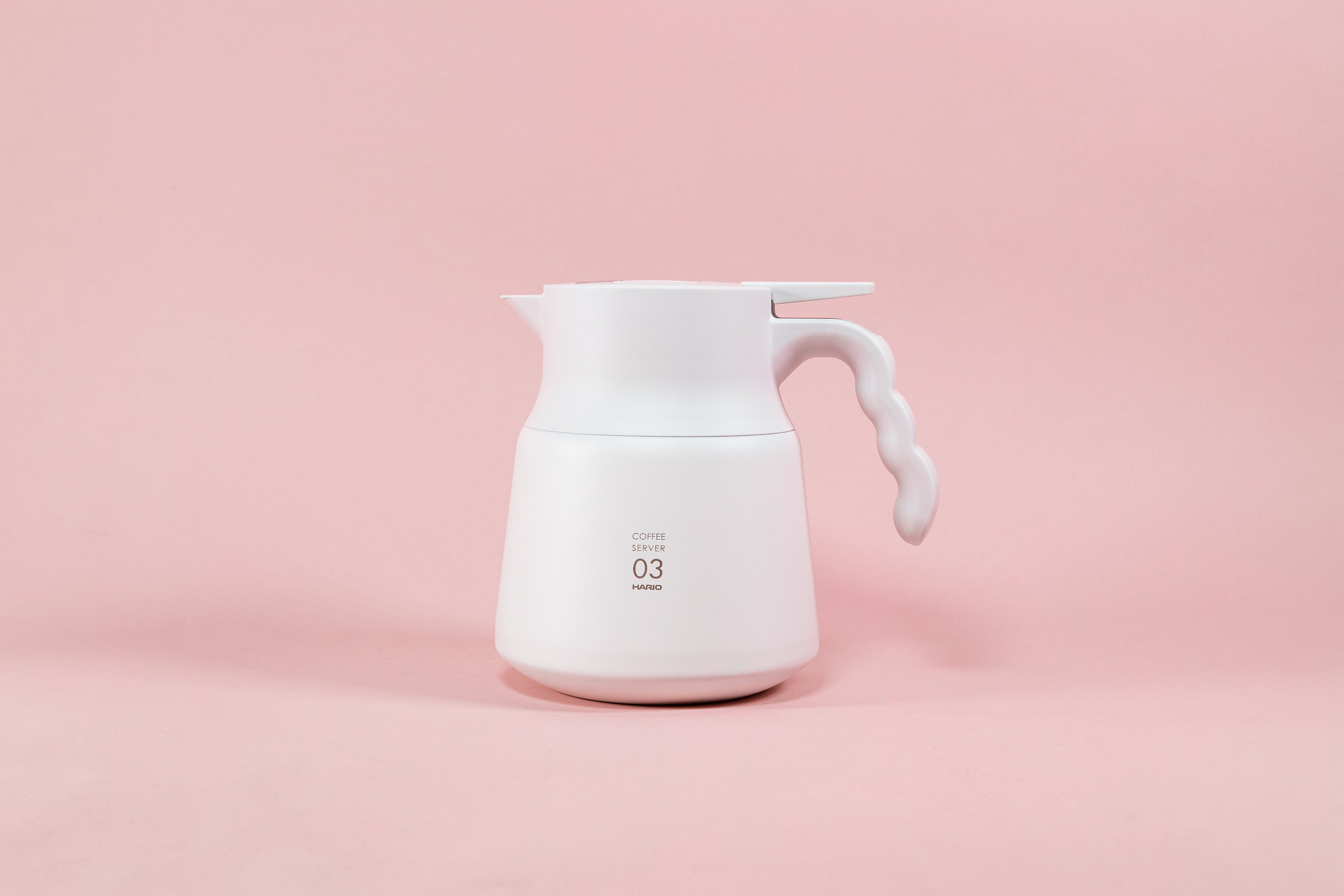 Matte white coffee server with wavy white plastic handle on a pink background.