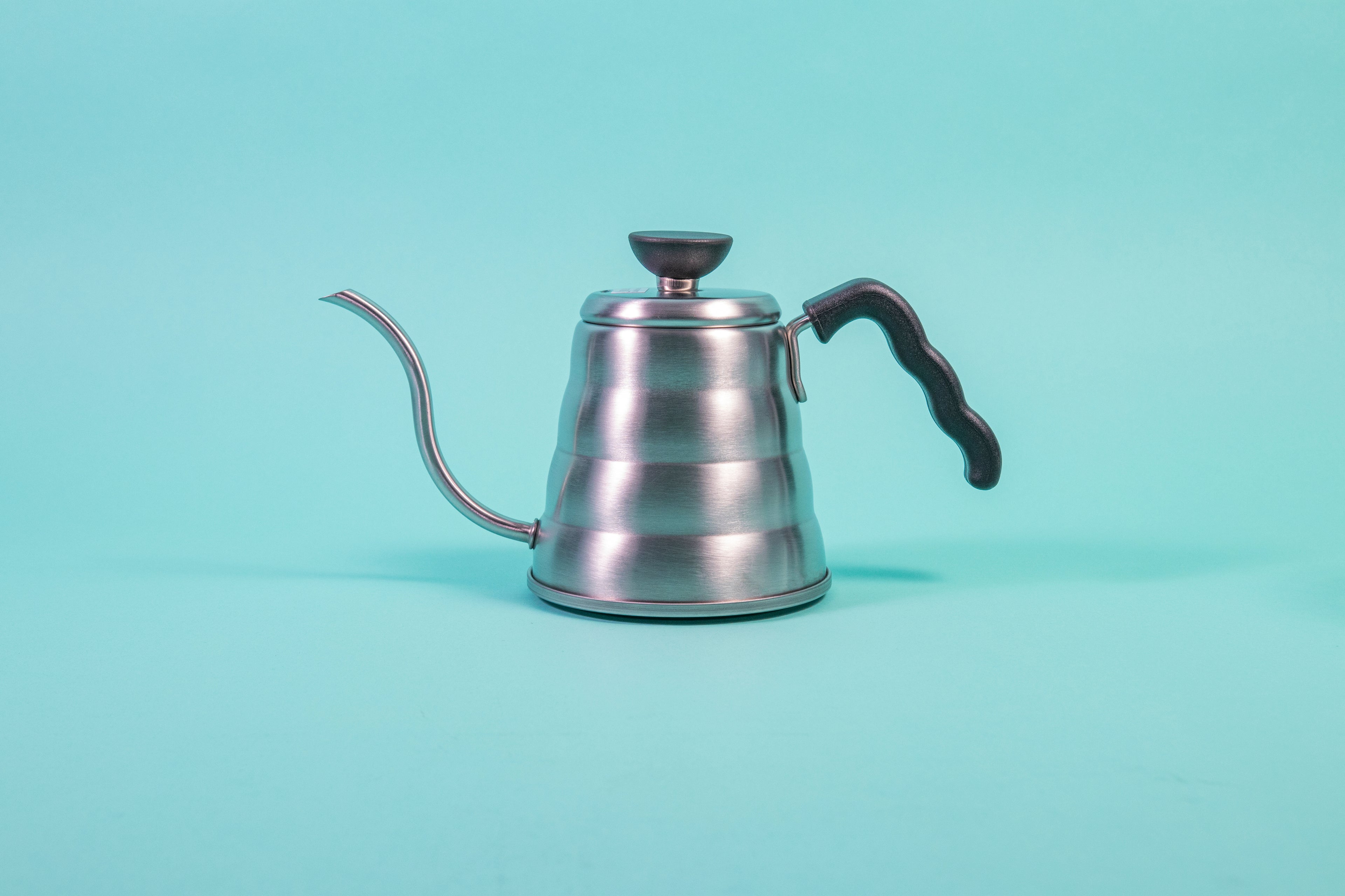 Silver beehive-shaped stainless steel kettle with wave-shaped black plastic handle and round black plastic lid knob with flat top set against a light blue background.