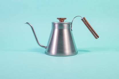 Stainless steel kettle with gooseneck spout, wood handle and flat, wood lid knob set against a light blue background.
