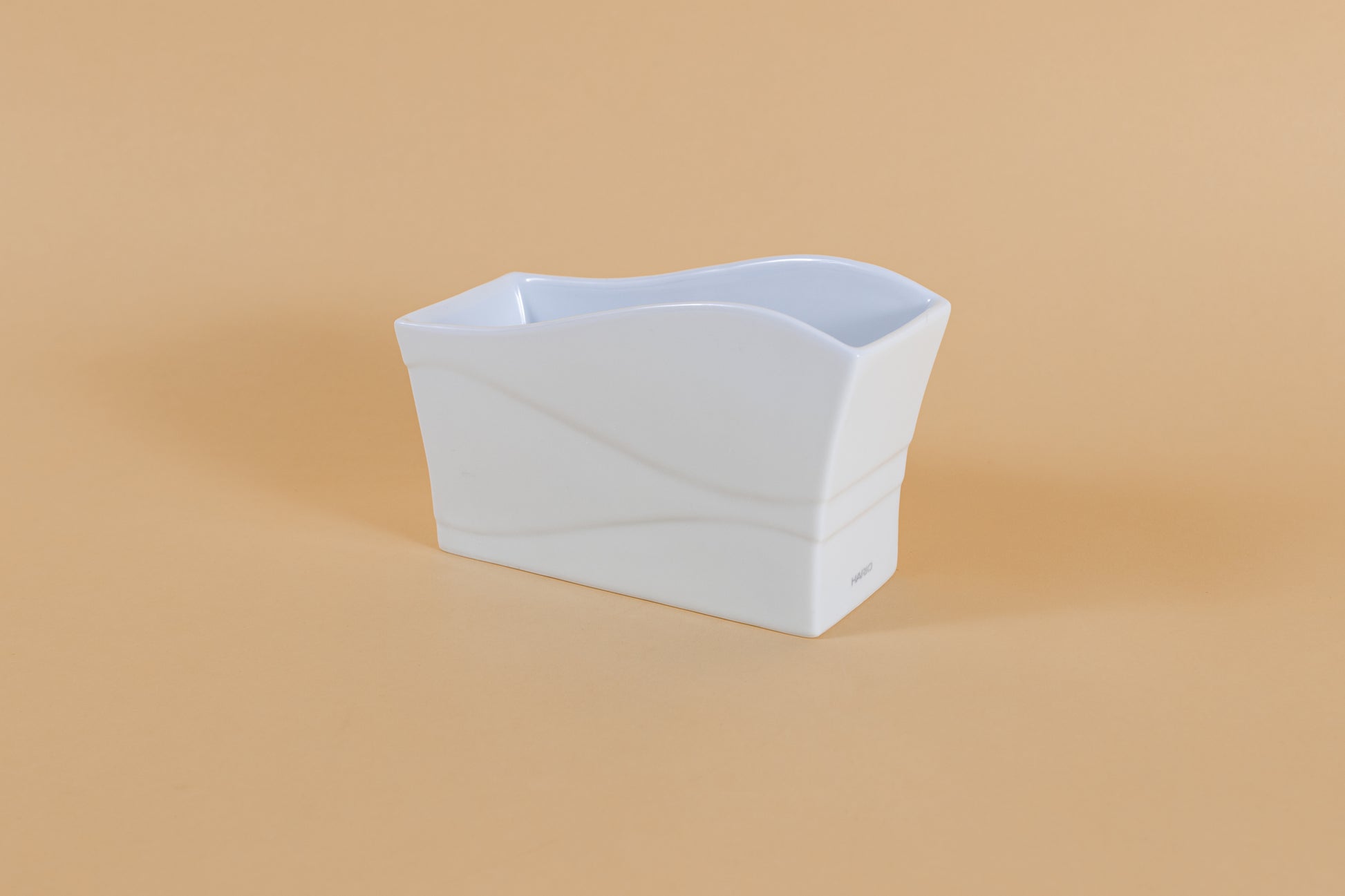 Rectangular all white ceramic vessel with "wave" design along side and top on orange backdrop.