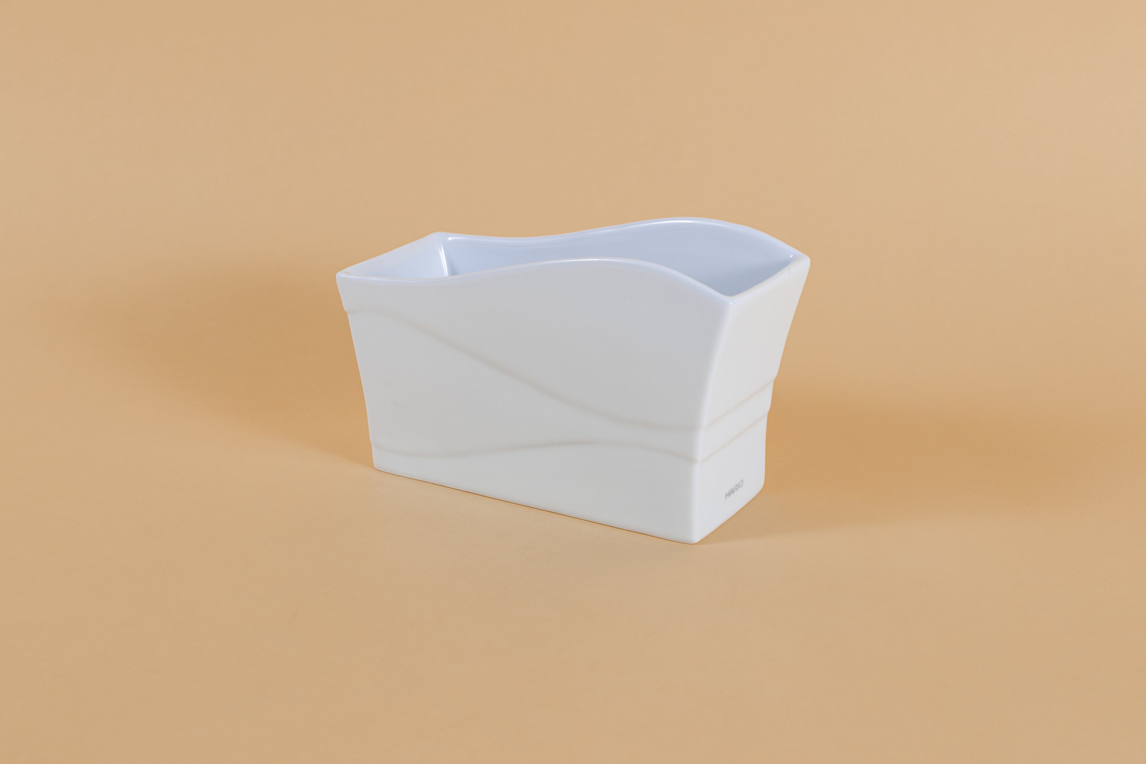 Rectangular all white ceramic vessel with &quot;wave&quot; design along side and top on orange backdrop.