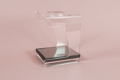 Clear acrylic stand with hole for cone dripper and black plastic drip with chrome screen on a pink backdrop.