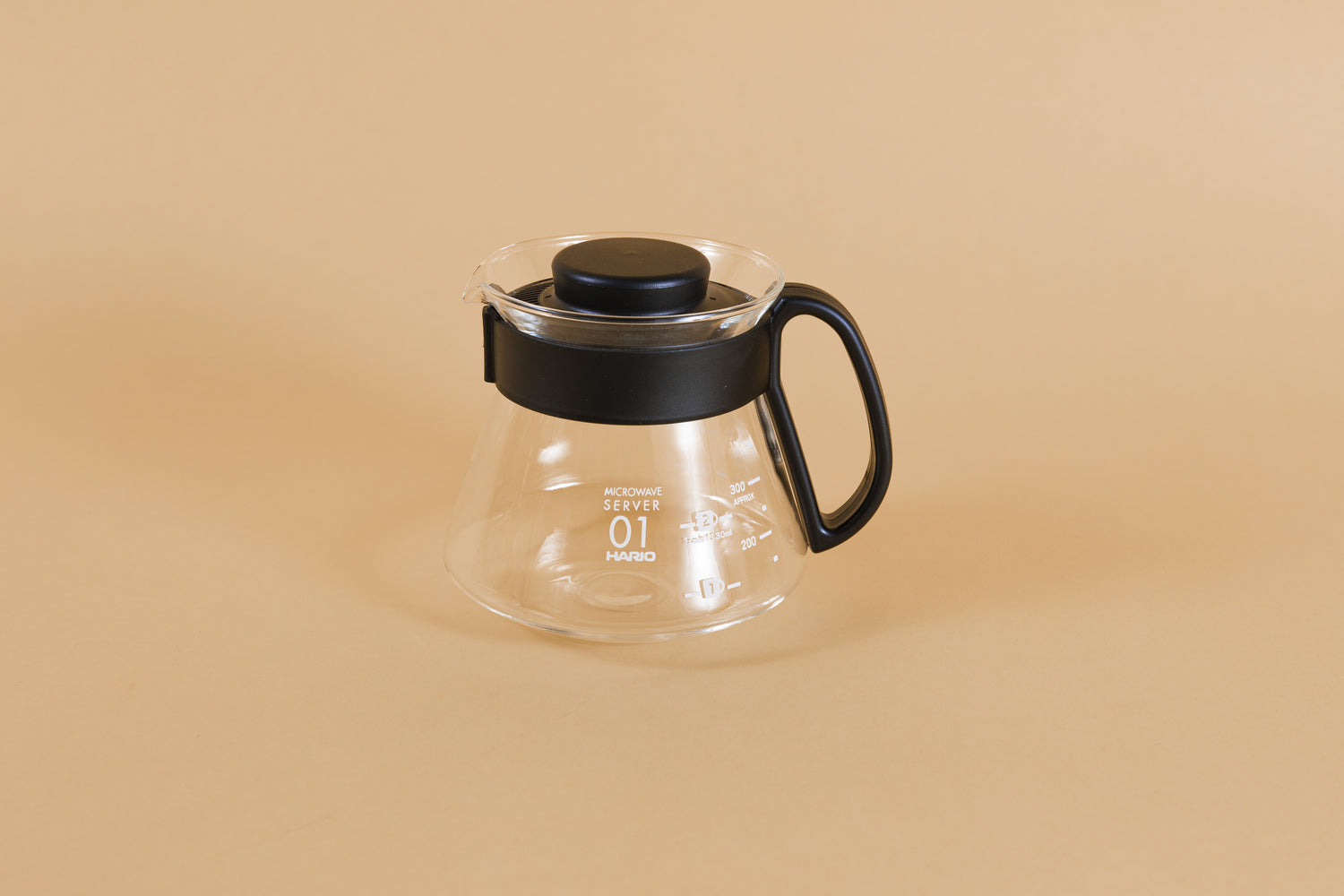 Glass coffee server with white text and level markings with closed black plastic handle and lid on an orange backdrop.