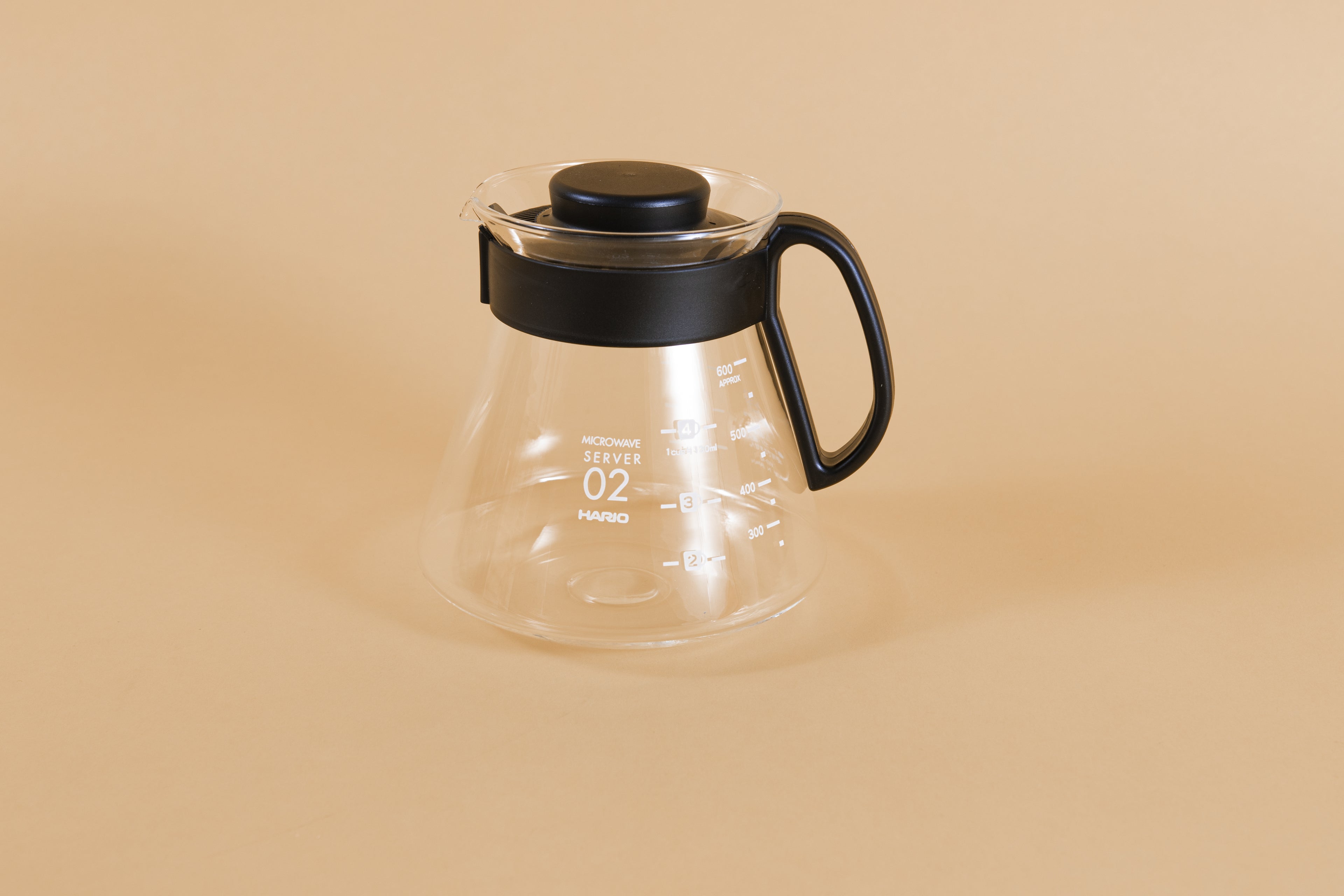 Glass coffee server with white text and level markings with closed black plastic handle and lid on an orange backdrop.