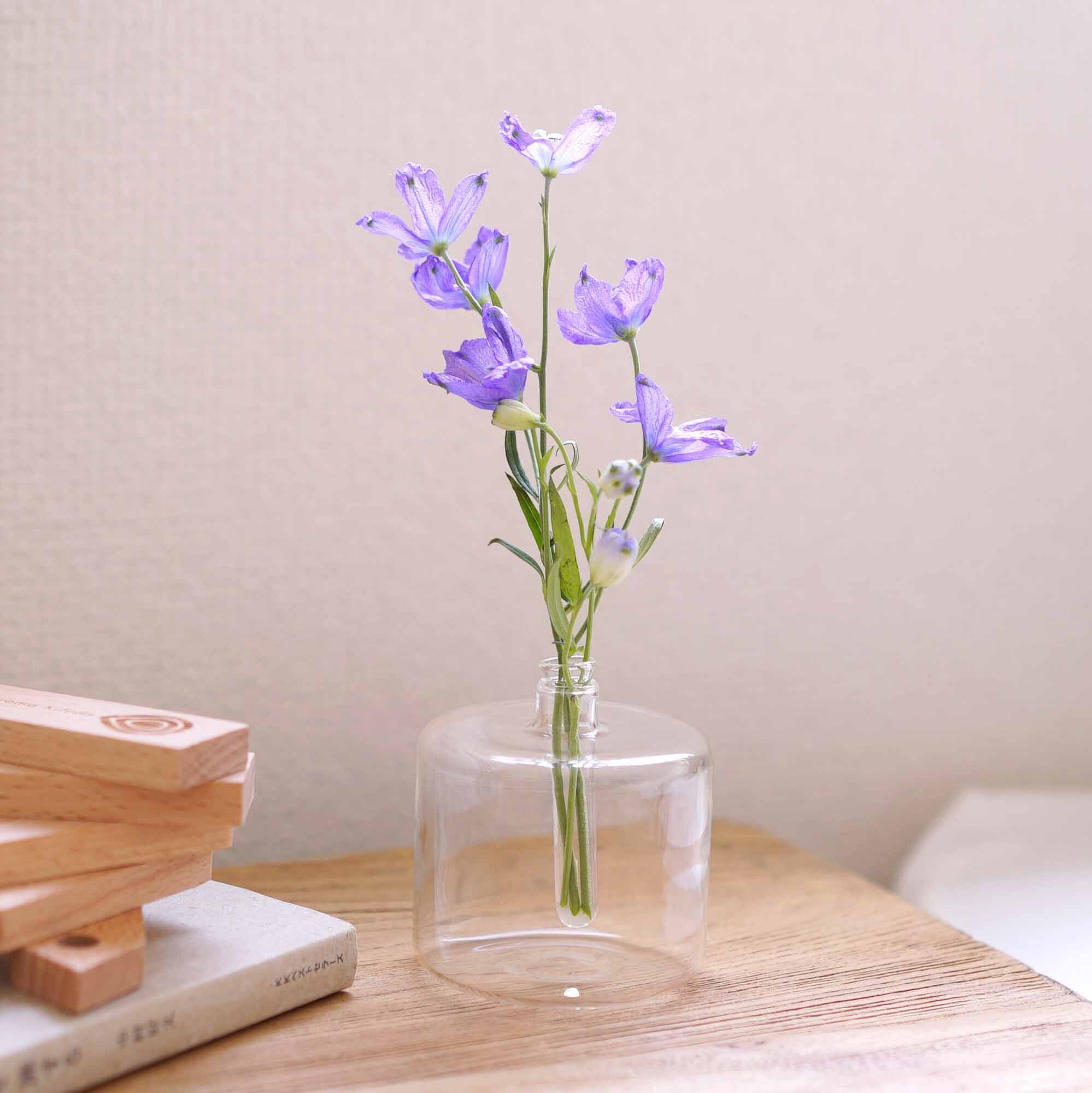 Round glass diffuser with purple flowers on a natural wood coffee table beside a white book and stacking blocks.